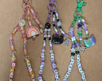 May include: Three beaded keychains with lobster claw clasps. The keychains feature colorful beads, charms, and the words "TO LOVE AND BE LOVED" spelled out in letter beads. One keychain has a rainbow charm.