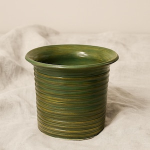 May include: A green ceramic vase with a textured, horizontal ridged design. The vase has a slightly flared rim and a cylindrical body. The color is a blend of green and yellow, creating a natural, earthy aesthetic. The vase is likely used for decorative purposes.