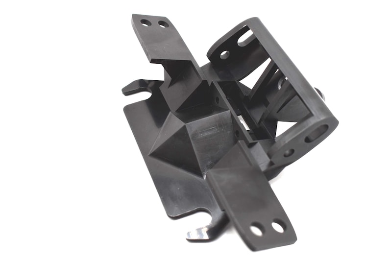 May include: A black, geometric plastic component with multiple arms and mounting holes. The object has a complex, angular design with a series of intersecting planes and a textured surface. The component appears to be a structural part.