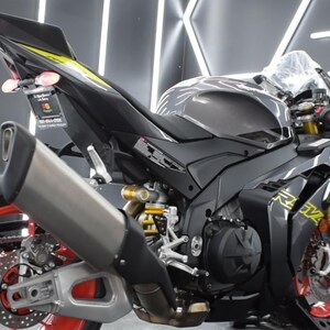 May include: A black and gray sport motorcycle with red accents on the wheels. The motorcycle has a silver exhaust pipe and yellow detailing. The image is a close-up of the rear and side of the motorcycle.