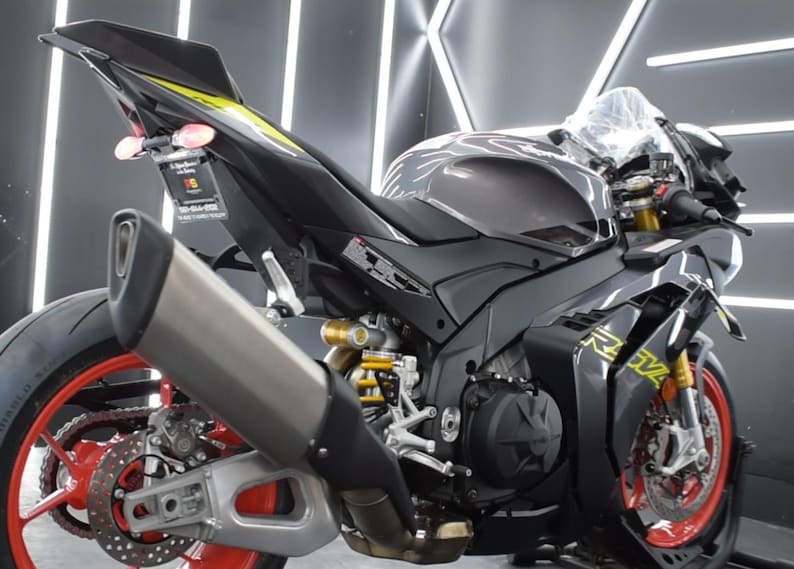 May include: A black and gray sport motorcycle with red accents on the wheels. The motorcycle has a silver exhaust pipe and yellow detailing. The image is a close-up of the rear and side of the motorcycle.