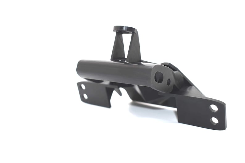 May include: A black, angular mechanical part with a cylindrical body and various mounting points. The part has a matte finish and is set against a white background, highlighting its geometric design and structural features.