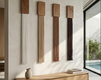 May include: Four vertical wall hangings, each featuring a rectangular wooden top piece with long, straight hanging cords in white, beige, light brown, and dark brown, arranged in a row above a low, light-toned wooden storage console unit.