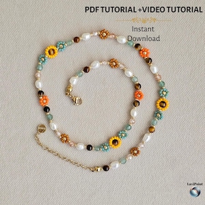 May include: A beaded necklace featuring white pearls, brown tiger eye beads, and small flower-shaped beads in yellow, orange, and teal. The necklace includes a gold-tone metal chain extender with a lobster clasp and a small round metal tag.