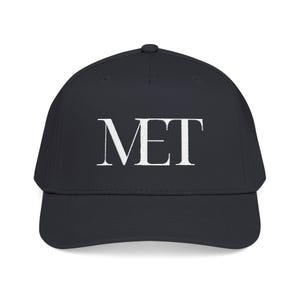 May include: A solid black baseball cap featuring the white embroidered text MET centered on the front panel. The cap has a structured crown, a curved brim, and a button at the top center. The design is clean and simple with a classic six-panel construction.