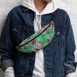 May include: A green fanny pack with a colorful pattern of red, white, and green shapes. The bag has a black strap and zipper. The fanny pack is worn across the body.