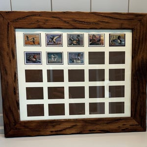 May include: A wooden framed display case with a natural finish. The case holds a collection of vintage stamps featuring birds in flight and on water. The frame has a rustic, textured appearance, and the stamps are arranged in rows.