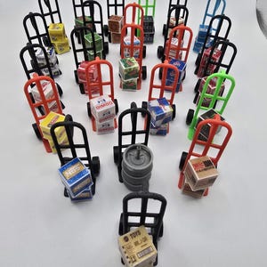 May include: A collection of miniature toy hand trucks in various colours, each carrying a small box. The boxes feature different brand logos and designs. The hand trucks are black, red, green, and blue.