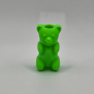 May include: A bright green, bear-shaped object with a hollowed-out top. The bear has rounded features, including ears, arms, and legs. The object is made of a solid material and is set against a plain background.