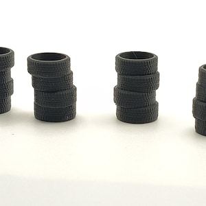 May include: Four stacks of small, black tires. Each stack consists of several tires, with visible tread patterns. The tires are arranged on a white surface, suggesting a miniature or model car theme.