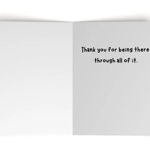 May include: A white greeting card opened to reveal a blank left side and a right side featuring the black printed text: Thank you for being there through all of it. The card has a clean, simple design with a matte finish and clear, dark lettering.