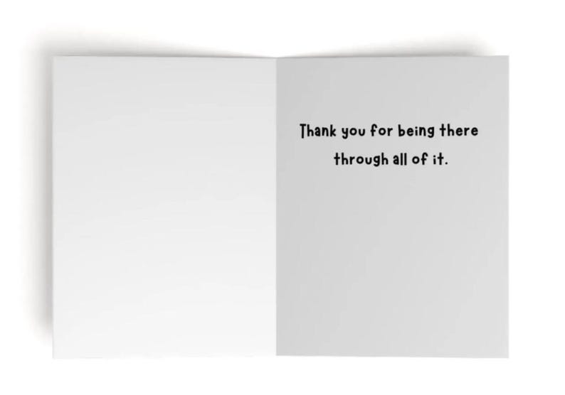May include: A white greeting card opened to reveal a blank left side and a right side featuring the black printed text: Thank you for being there through all of it. The card has a clean, simple design with a matte finish and clear, dark lettering.