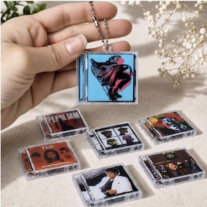 May include: A collection of miniature square clear plastic cases resembling CD jewel cases, each featuring iconic album cover art including Pearl Jam, TLC, and Michael Jackson. One case is attached to a silver ball chain keychain.