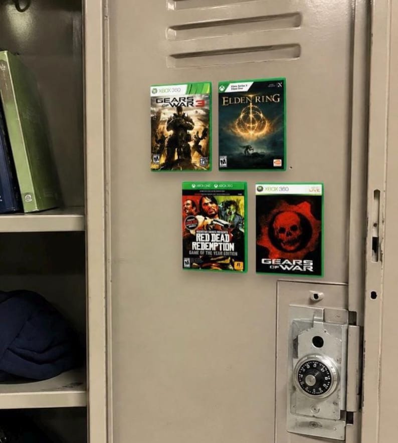 May include: Four video game cases attached to a beige metal locker door. The titles include Gears of War 3, Elden Ring, Red Dead Redemption Game of the Year Edition, and Gears of War. Each case features its respective cover art and console branding.