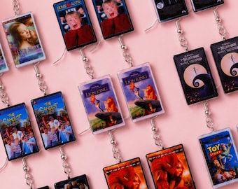 May include: A collection of rectangular dangle earrings featuring miniature replicas of classic movie VHS covers including Home Alone, The Lion King, The Sandlot, The Nightmare Before Christmas, Spider-Man 2, and Toy Story, attached to silver-toned hooks.