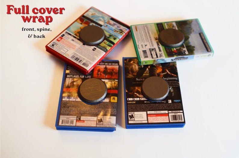 May include: Four rectangular video game cases with full cover wraps featuring front, spine, and back artwork. Each case has a circular dark gray magnet attached to the center of the back cover. The cases are arranged in a cluster on a plain surface.
