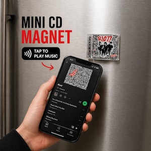 May include: A mini CD magnet featuring the album art for "Riot!" by Paramore. The magnet is displayed on a refrigerator next to a smartphone displaying the album art and song list. The text "MINI CD MAGNET" and "TAP TO PLAY MUSIC" are also visible.