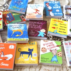 May include: A collection of miniature book keychains featuring various children's storybook covers including The Cat in the Hat, Green Eggs and Ham, Pete the Cat, The Smart Cookie, If You Give a Mouse a Cookie, and Harold and the Purple Crayon.