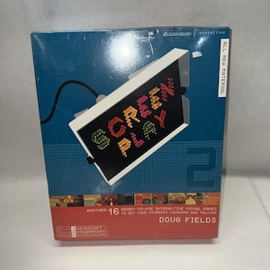 May include: A rectangular product box for Screen Play 2 by Doug Fields, featuring a blue and red background with a white frame graphic containing colorful text. The box includes text stating 16 ready-to-use interactive visual games and Microsoft PowerPoint player included.