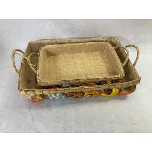 May include: A set of two rectangular woven baskets with rope handles. The baskets feature a natural tan fiber texture and are decorated along the exterior base with a row of colorful, glossy, fruit-shaped accents in red, yellow, orange, and blue.