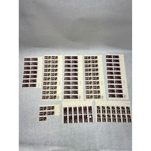 May include: A collection of multiple sheets of postage stamps featuring a dark rectangular design with a central illustration and text. The stamps are arranged in vertical and horizontal strips on off-white backing paper, showing various quantities per sheet.