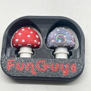 May include: Two mushroom-shaped glass plugs in a black plastic case with the word "Fun Guys" printed in red. One plug is red with white polka dots, the other is iridescent with white swirls.