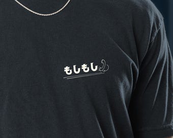 May include: Dark navy blue t-shirt with the Japanese phrase "Moshi Moshi" printed in white. The shirt has a small, minimalist design and a classic crew neck.