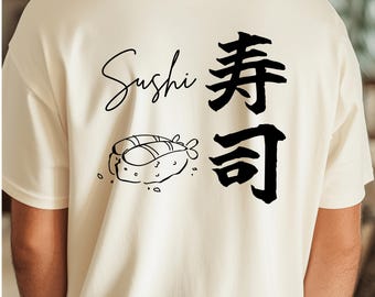 May include: Cream-colored t-shirt featuring the word "Sushi" in a cursive font, accompanied by Japanese characters and a sushi illustration. The design is in black ink, creating a minimalist aesthetic.