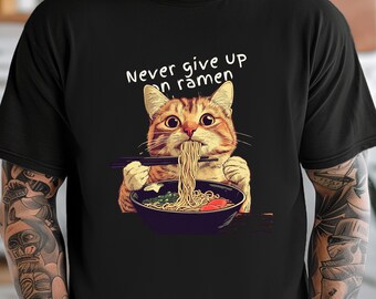 May include: A black t-shirt with a graphic of a cat eating ramen noodles. The text "Never give up on ramen" is printed on the shirt.