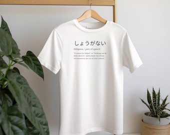 May include: White t-shirt with a Japanese word and definition printed on the front. The word is "しょうがない" and the definition is "Shoganai/part-of-speech "It cannot be helped" or "Nothing can be done about it." particularly one whose circumstances are out of your control."