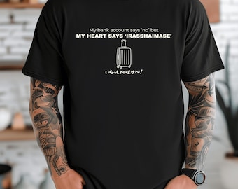May include: Black t-shirt with white text and a suitcase graphic. The text reads "My bank account says 'no' but MY HEART SAYS 'IRASSHAIMASE'" with Japanese text below. A travel-themed graphic tee.
