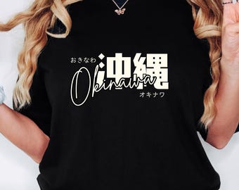 May include: Black t-shirt with white text that says "Okinawa" in a cursive font. The text is surrounded by Japanese characters that say "Okinawa" and "Okinawa".