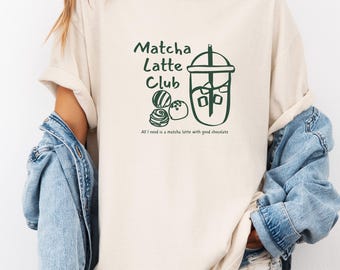 May include: A beige t-shirt with a green graphic of a matcha latte with chocolate. The text on the shirt reads "Matcha Latte Club" and "All I need is a matcha latte with good chocolate."