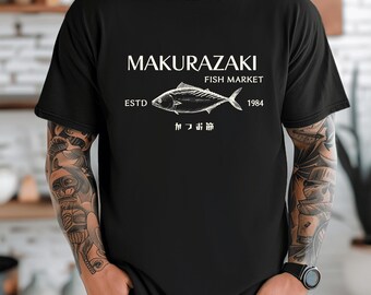 May include: Black t-shirt featuring a white graphic of a fish and the text "MAKURAZAKI FISH MARKET ESTD 1984". Below the fish is Japanese text. The shirt is a crew neck style.