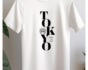May include: White t-shirt with a black graphic design of the word "TOKYO" with a stylized image of a Japanese guardian lion in the middle of the word. The text "Family Trip 2025" is below the graphic.