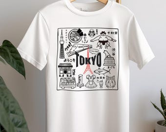 May include: White t-shirt with a black and white illustration of various Tokyo landmarks, including the Tokyo Skytree, a sushi restaurant, a sumo wrestler, and the iconic red and white Tokyo Tower. The text "TOKYO" is printed in bold red letters.