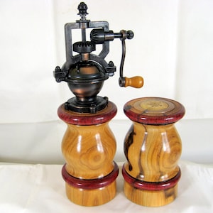 May include: A wooden salt and pepper grinder set. The pepper grinder has a dark metal mechanism with a wooden handle. The salt shaker and pepper grinder have a light brown wooden base with a red accent.
