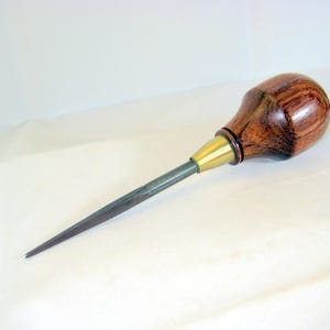 May include: A hand tool with a wooden handle and a metal tip. The handle is a dark brown color with visible wood grain. The metal tip is a dark gray color. The tool has a brass-colored collar where the handle meets the metal tip.