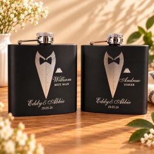 Könnte beinhalten: Zwei mattschwarze Metallflachmänner mit einer silbernen Gravur im Smoking-Design. Der linke Flachmann ist mit William, BEST MAN, Eddy & Abbie und 28.05.26 graviert. Der rechte mit Andrew, USHER, Eddy & Abbie und 28.05.26.