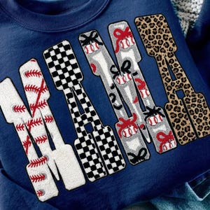 Pode incluir: Camisola azul marinho com a palavra "MAMA" em vários padrões. O "M" é branco com costuras de basebol vermelhas, o primeiro "A" é xadrez preto e branco, o segundo "M" é cinzento com bolas de basebol e laços vermelhos, e o último "A" é estampado de leopardo.