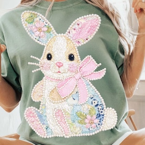 Op de afbeelding: Saliegroen sweatshirt met een geborduurd konijnontwerp. Het konijn heeft een wit gezicht, een roze strik en bloemendetails op de oren en het lichaam. Het ontwerp is versierd met kleine, parelachtige kralen.