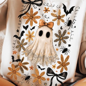May include: Cream-coloured sweatshirt with a Halloween design. The graphic features a ghost with a bow, flowers, spiders, and bats. The words "digital download" are printed on the bottom right. The Infinite Pixel studio logo is on the bottom left.