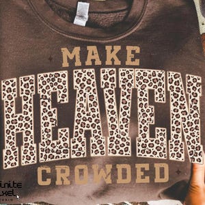 May include: A brown sweatshirt with the words "MAKE HEAVEN CROWDED" in a bold, leopard print design. The sweatshirt is held up by hands, showcasing the text prominently. The overall style is casual and trendy.