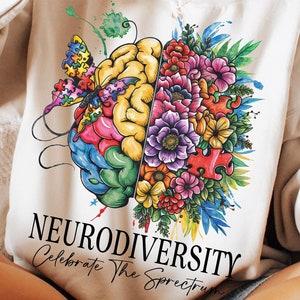 May include: A white sweatshirt with a colorful brain and flower design. The brain is half puzzle pieces and half flowers. The text "Neurodiversity Celebrate The Spectrum" is printed on the bottom of the sweatshirt.