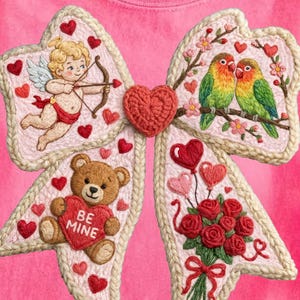 Puede incluir: Camiseta rosa con un gran diseño de lazo bordado. El lazo está decorado con un cupido, un oso de peluche con un corazón que dice "Be Mine", pájaros del amor, corazones y rosas. La camiseta está hecha de un material suave.