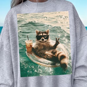 Immagine PNG di un simpatico procione estivo, grafica di un animale galleggiante da spiaggia, stampa divertente per maglietta con atmosfera vacanziera, download per sublimazione per feste in piscina alla moda