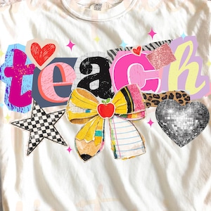 Puede incluir: Camiseta color crema con la palabra "TEACH" en un estilo collage colorido. El diseño incluye un lazo de lápiz, una estrella a cuadros, un corazón de bola de discoteca y un acento de estampado de leopardo. La camiseta es de la marca Comfort Colors.