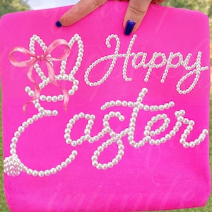 May include: A bright pink sign with the words "Happy Easter" written in white pearl-like beads. A pink bow and pearl accents adorn the upper left corner. The sign is held up by a hand with blue nail polish.