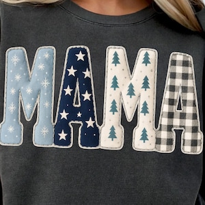 May include: Dark gray sweatshirt with the word "MAMA" in large, decorative letters. The letters are patterned with snowflakes, stars, Christmas trees, and a black and white plaid design.