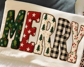 Può includere: Una felpa color crema a tema natalizio con la scritta "MERRY" in grandi lettere decorative. Ogni lettera presenta un motivo festivo diverso: agrifoglio, stelle, alberi di Natale, quadri a quadri e bacche. La felpa è su una superficie bianca e soffice.